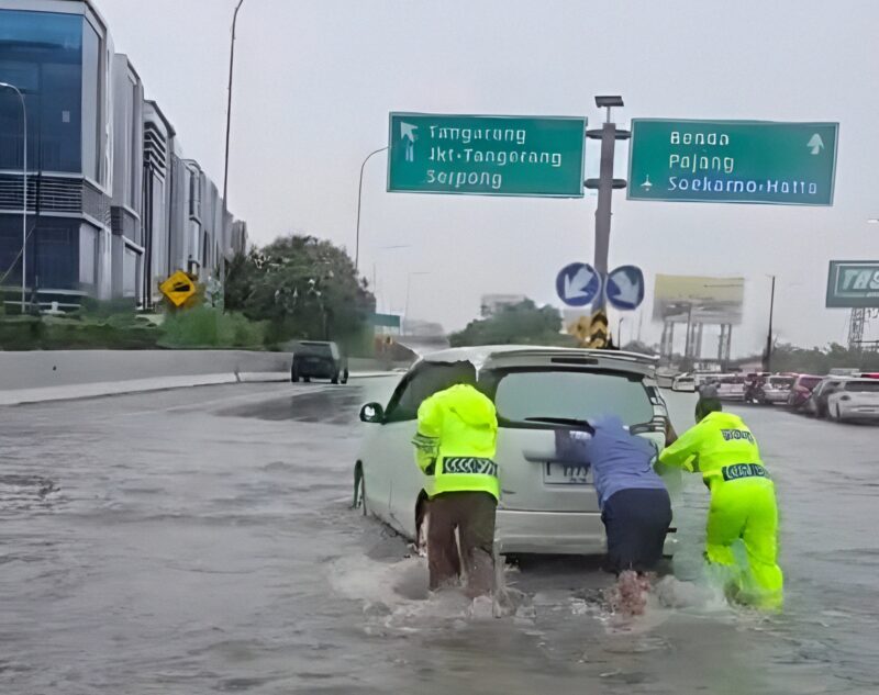 Petugas Satlantas Bandara Soekarno-Hatta sedang mendorong mobil mogok di ruas Jalan Tol menuju Bandara Internasional Soekarno-Hatta yang terendam banjir pada Senin (12/1/2026).(Foto: Dok.TMC Polda Metro Jaya)