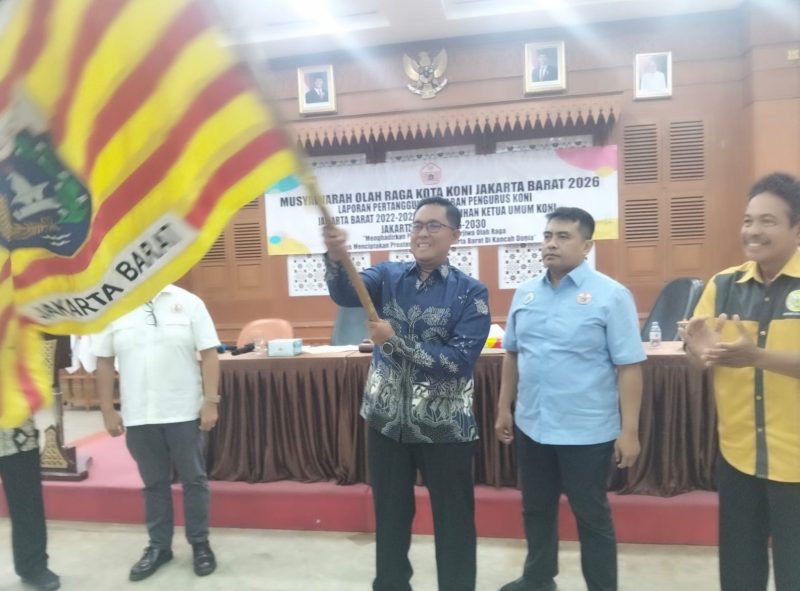 Agus Ramdani mengibarkan pataka usai ditetapkan sebagai Ketua KONI Jakarta Barat periode 2026-2030 dalam Musorkot di Ruang Ali Sadikin, Kantor Wali Kota Jakarta Barat, Senin (27/4/2026). (Foto: istimewa)